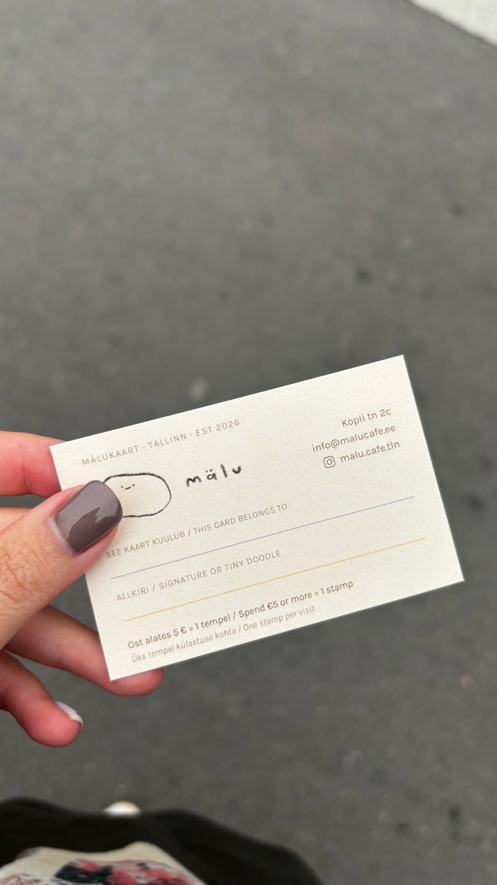 A hand holding the mälu cafe loyalty card against a gray pavement